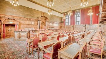 An empty council chamber with rows of wooden seats